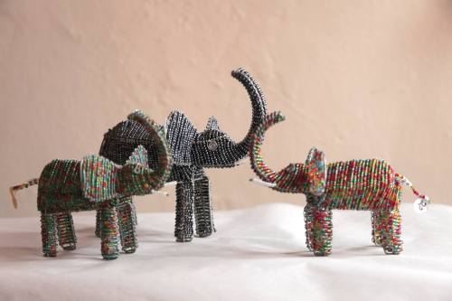 Three colorful wire elephants in various poses, showcasing intricate beadwork and craftsmanship against a neutral background.
