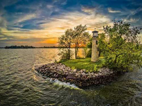 A scenic lighthouse on a small island at sunset, surrounded by water and lush greenery.