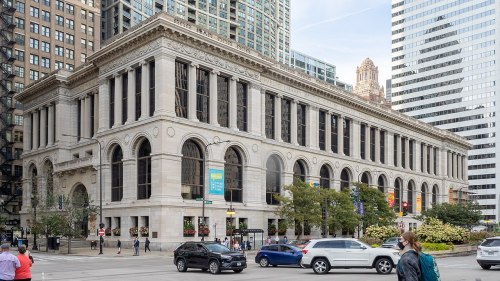 A historic building with large windows and arches, surrounded by modern skyscrapers and greenery in an urban setting.