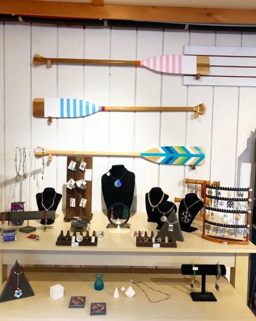 Display of various jewelry pieces on stands, with decorative paddles hanging above in a bright, inviting shop setting.