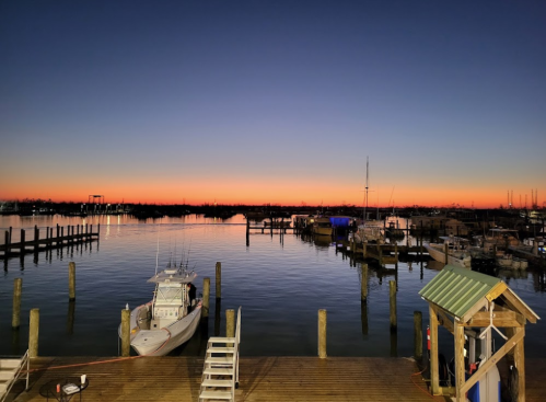 A serene harbor at sunset, with boats docked and a colorful sky reflecting on calm waters.