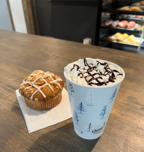 A cozy coffee shop scene featuring a muffin and a cup of hot chocolate topped with whipped cream and chocolate drizzle.