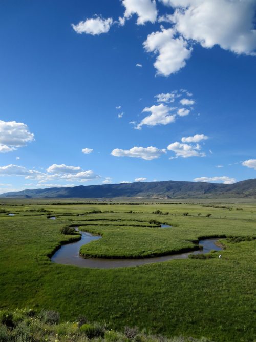 A winding river flows through a lush green landscape under a bright blue sky with fluffy white clouds.