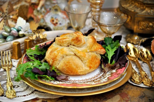 A beautifully plated pastry dish on an ornate table setting, surrounded by greens and elegant glassware.