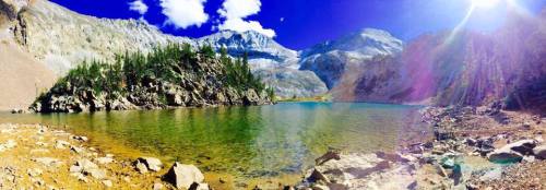 A serene mountain lake surrounded by rocky terrain and lush greenery, under a bright blue sky with scattered clouds.
