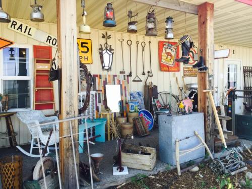 A rustic display of vintage items, including lanterns, tools, and signs, arranged on a porch.