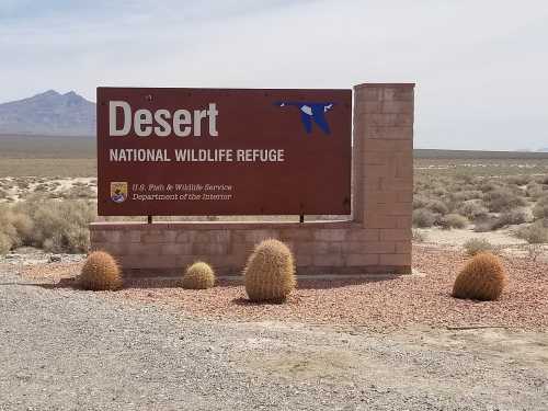 Sign for Desert National Wildlife Refuge, featuring a blue bird graphic and surrounded by desert landscape and cacti.