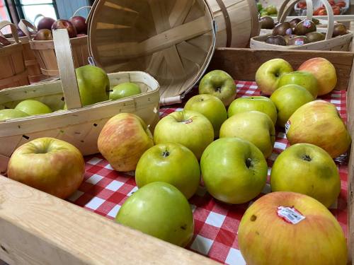 A variety of apples, including green and red, arranged on a checkered tablecloth near wooden baskets.