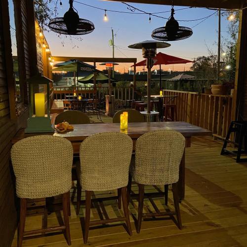 Cozy outdoor dining area at dusk, featuring wooden tables, woven chairs, and soft lighting under a colorful sky.