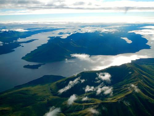 Aerial view of lush green mountains and islands surrounded by calm blue waters and scattered clouds.