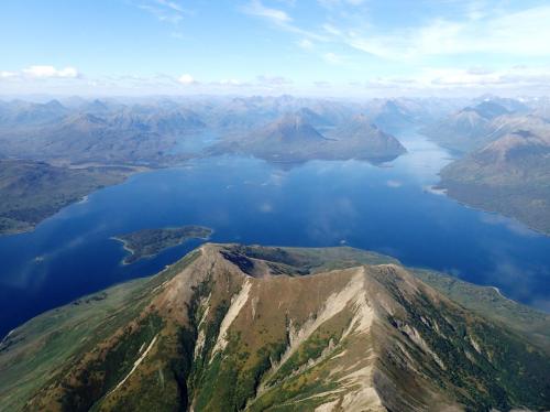 Aerial view of a vast lake surrounded by mountains and lush greenery under a clear blue sky.
