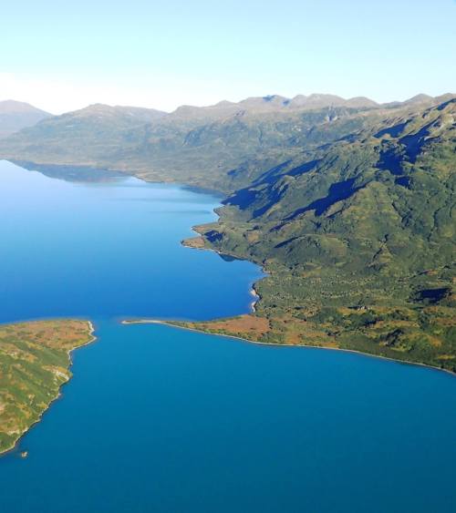 Aerial view of a serene lake surrounded by lush green mountains under a clear blue sky.