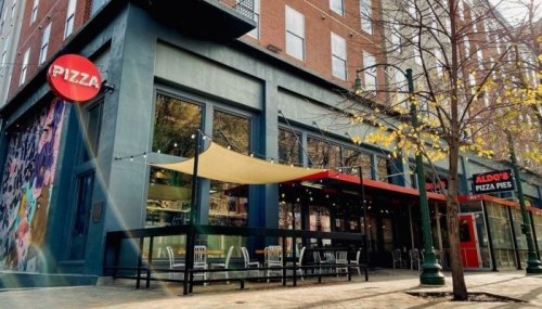 Exterior view of a pizza restaurant with a colorful mural, outdoor seating, and a nearby sign for Aldo's Pizza Pies.