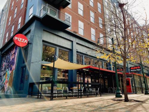 Exterior of a pizza restaurant with large windows, outdoor seating, and a colorful mural on the side.