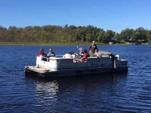 A group of people enjoying a sunny day on a pontoon boat on a calm lake surrounded by trees.