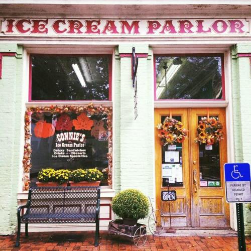 A charming ice cream parlor with a green exterior, decorated for fall, featuring a bench outside and an "Open" sign.