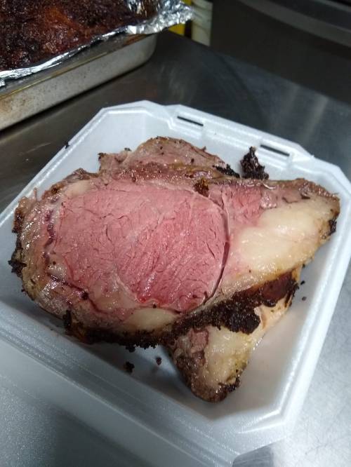 A slice of medium-rare roast beef on a white takeout container, showcasing a pink center and crispy edges.