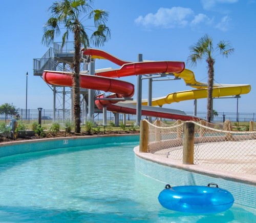 Colorful water slides beside a clear pool, with palm trees and a sunny blue sky in the background.