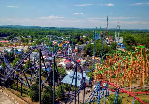 Aerial view of a vibrant amusement park featuring roller coasters, rides, and lush green surroundings.