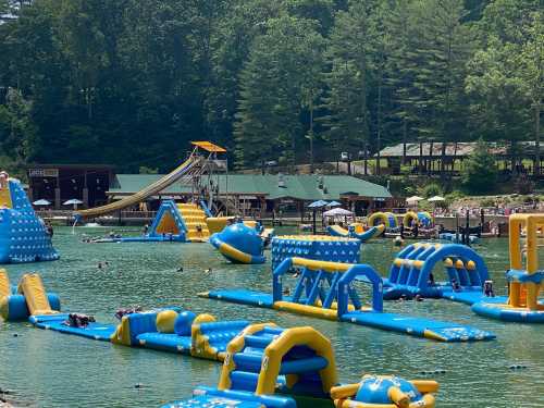 A vibrant water park with inflatable structures on a lake, surrounded by trees and people enjoying the sun.