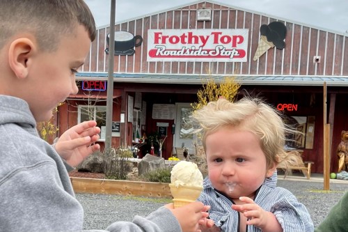 Two young children outside a roadside ice cream shop, one holding an ice cream cone, the other looking surprised.