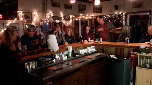 A lively bar scene with patrons chatting and enjoying drinks, decorated with string lights and a warm atmosphere.