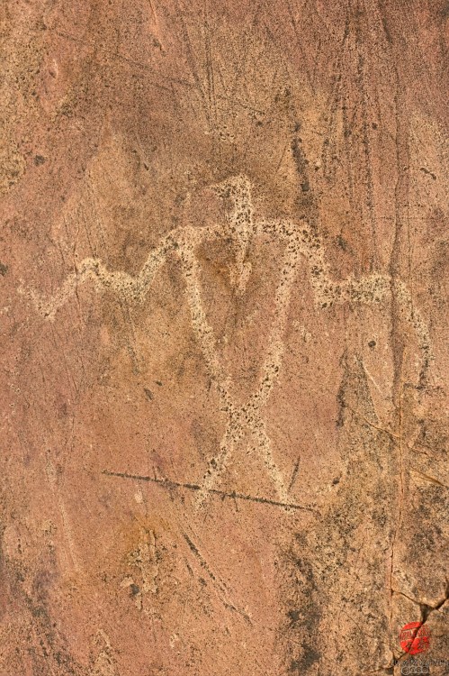 Petroglyph of a humanoid figure with outstretched arms, etched into a rocky surface.