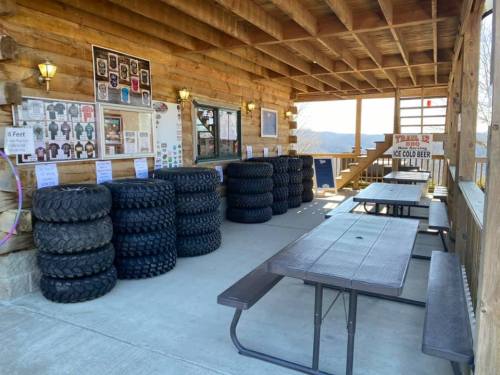A rustic outdoor seating area with stacked tires, picnic tables, and a wooden structure in a scenic location.
