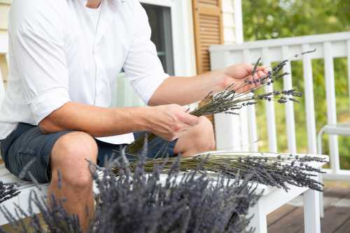 A person in a white shirt sits on a porch, arranging bundles of lavender flowers.