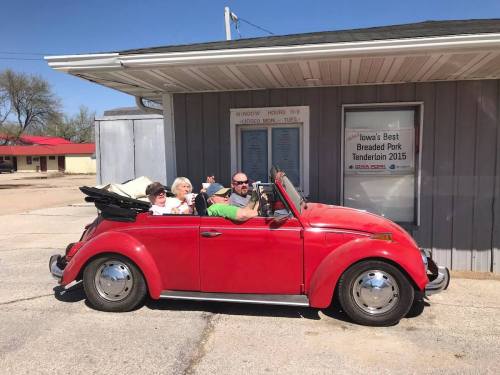A red convertible parked outside a building, with three people smiling and posing for the photo.
