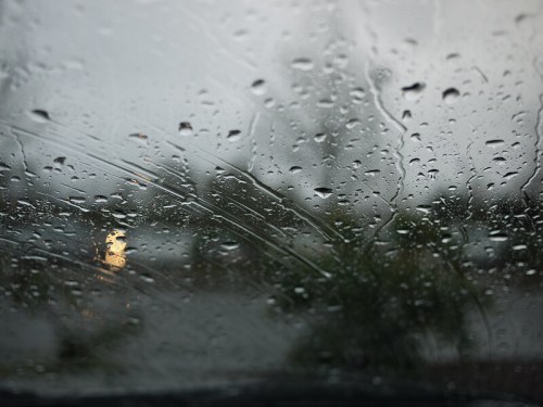 Raindrops on a car window, blurring the view of a dimly lit scene outside.