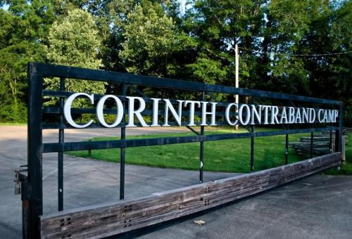 Sign for Corinth Contraband Camp, surrounded by trees and greenery, marking a historical site.