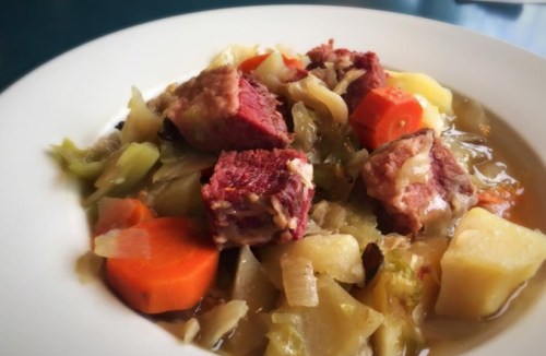 A bowl of hearty soup with chunks of meat, cabbage, carrots, and potatoes in a savory broth.