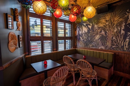 Cozy restaurant corner with colorful pendant lights, wooden seating, and tropical-themed wall decor.