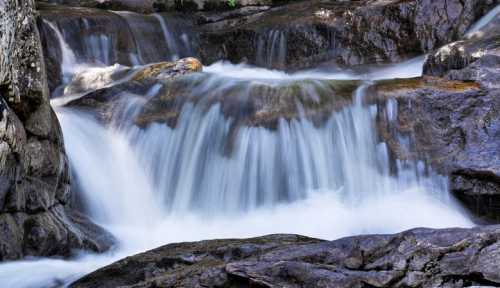 A serene waterfall cascading over smooth rocks, surrounded by lush greenery.