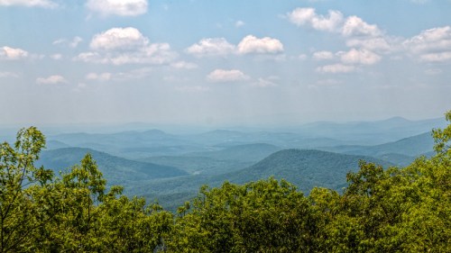 A panoramic view of rolling green mountains under a blue sky with fluffy white clouds.