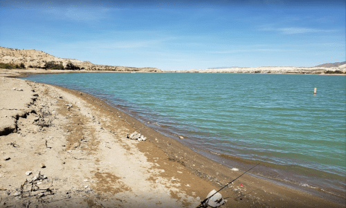 A serene lakeside view with sandy shores and calm turquoise water under a clear blue sky.
