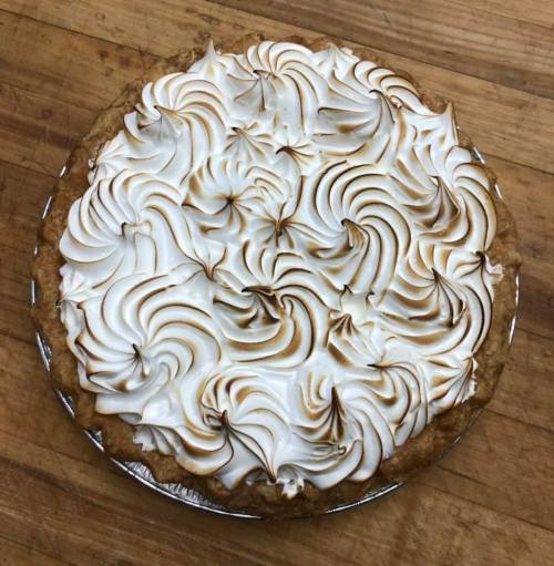 A beautifully baked pie topped with swirls of golden-brown meringue on a wooden surface.