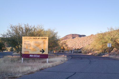 Sign for Deer Valley Rock Art Center at Arizona State University, with desert landscape and mountains in the background.