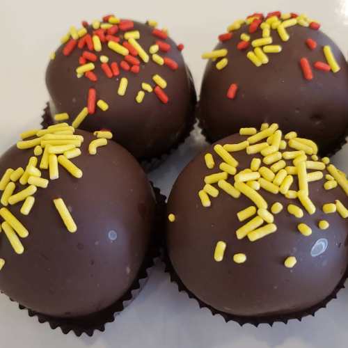 Four chocolate-covered treats topped with red and yellow sprinkles, arranged on a white plate.