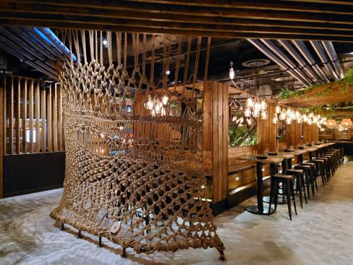 A modern restaurant interior featuring wooden decor, a rope partition, and stylish lighting.