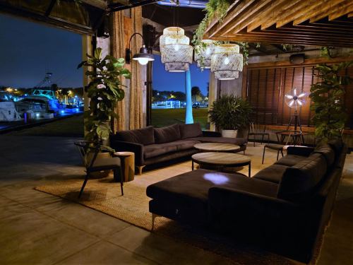 Cozy outdoor lounge area at night with plants, modern furniture, and decorative lighting overlooking a waterfront.