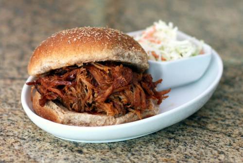A pulled pork sandwich on a sesame seed bun, served with a side of coleslaw on a white plate.