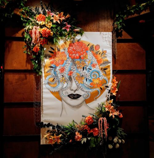 A vibrant mural of a woman's face adorned with colorful flowers and intricate patterns, framed by lush greenery.