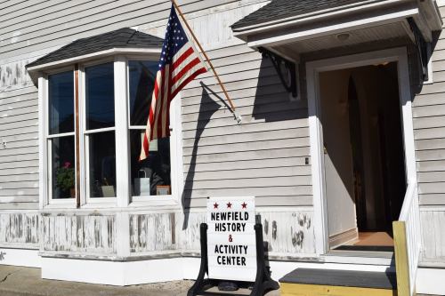 Exterior of the Newfield History & Activity Center, featuring an American flag and a welcoming entrance.