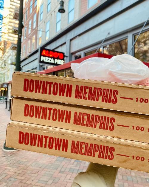 Three pizza boxes stacked with "DOWNTOWN MEMPHIS" printed on them, in front of Aldo's Pizza Pies restaurant.