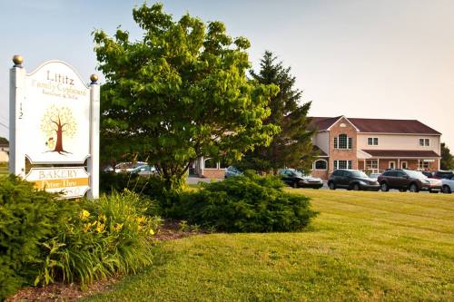 A bakery sign in front of a green landscape, with a building and parked cars in the background.
