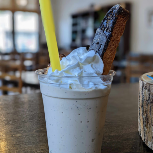 A creamy milkshake topped with whipped cream and a chocolate cookie, served in a clear cup with a yellow straw.