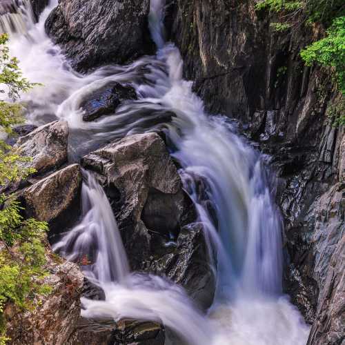 A cascading waterfall flows over rocky terrain, surrounded by lush green foliage.