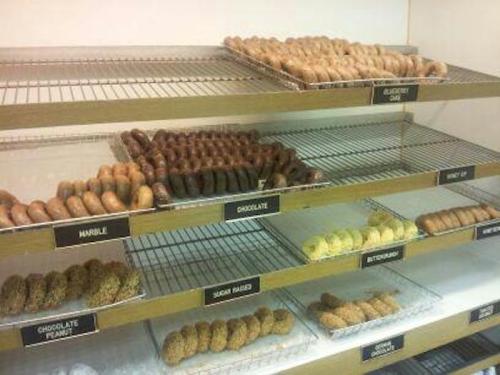A display of various donuts on racks, including glazed, chocolate, and peanut varieties, labeled for selection.